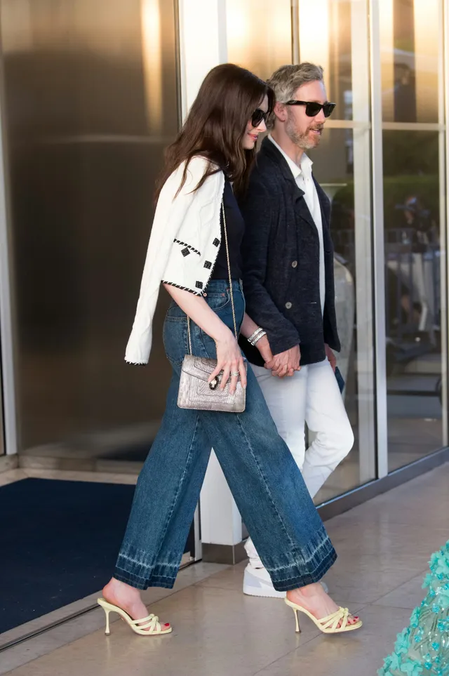 Anne Hathaway walking outside in jeans and pale heels.