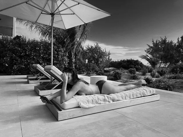 Josephine Skriver reclining barefoot on a lounger beneath a parasol.