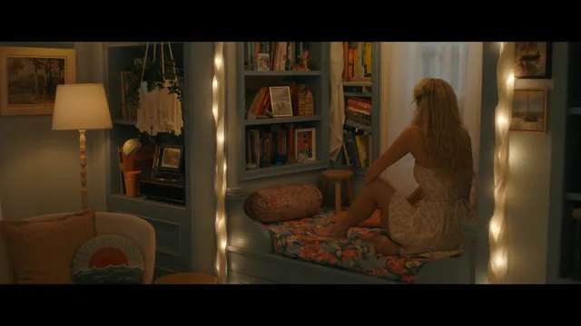 Emily Alyn Lind sitting cross-legged barefoot in a patterned dress at a dressing table.