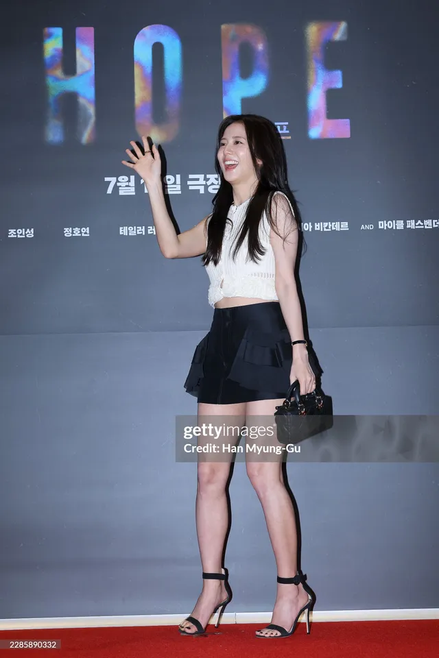 Jisoo waving while wearing black heels, a white top and a short dark skirt.