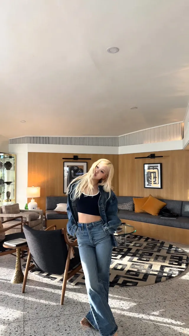 Rosé leaning her head to one side in a cropped top and jeans in an indoor lounge.