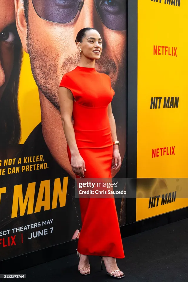 Adria Arjona wearing a red dress and pale heels at a film premiere.