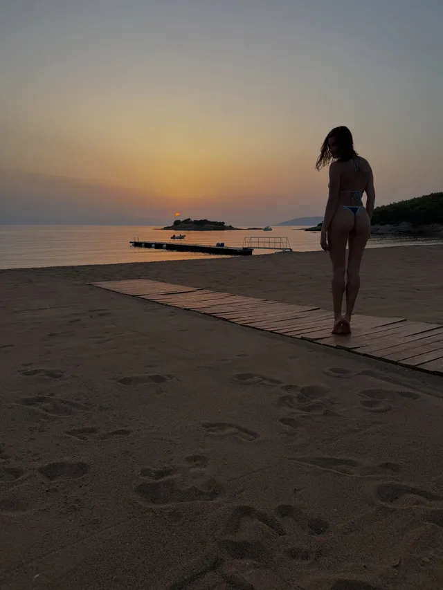 Hailey Bieber walking barefoot beside the sea at sunset.