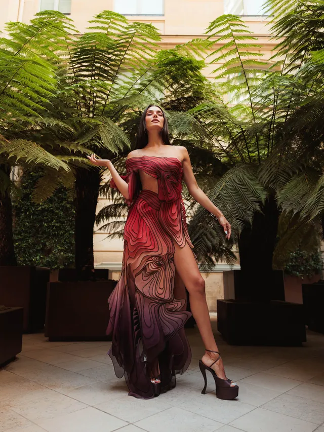 Hande Erçel posing outdoors in a long patterned gown and platform heels.
