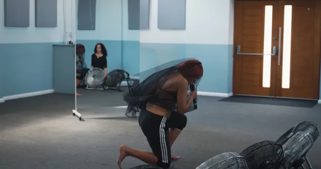 Naomi Scott kneeling barefoot beside floor fans.