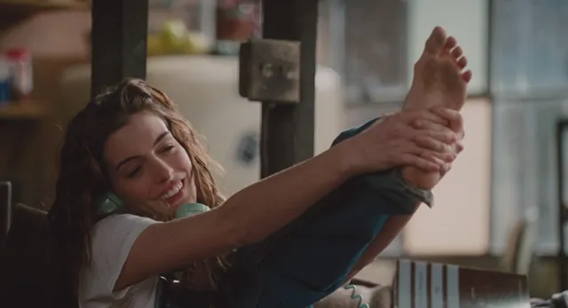 Anne Hathaway stretching with a bare foot held in both hands.