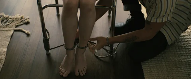 Sophie Thatcher having an ankle accessory adjusted in a film scene.