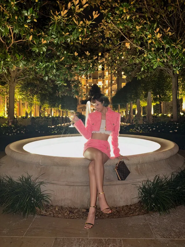 Lisa (Lalisa Manobal) sitting on a garden ledge in gold heels and a pink outfit.