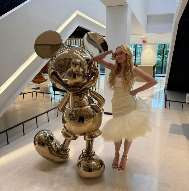 Lindsay Lohan posing in a white dress beside a gold statue.