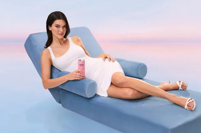 Kendall Jenner reclining in a white dress and white sandals.