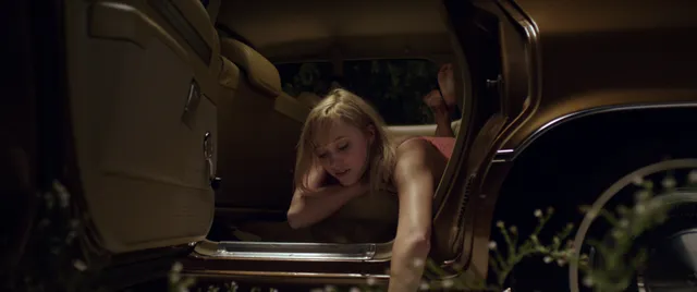 Maika Monroe reaching barefoot out of a vehicle in a scene.
