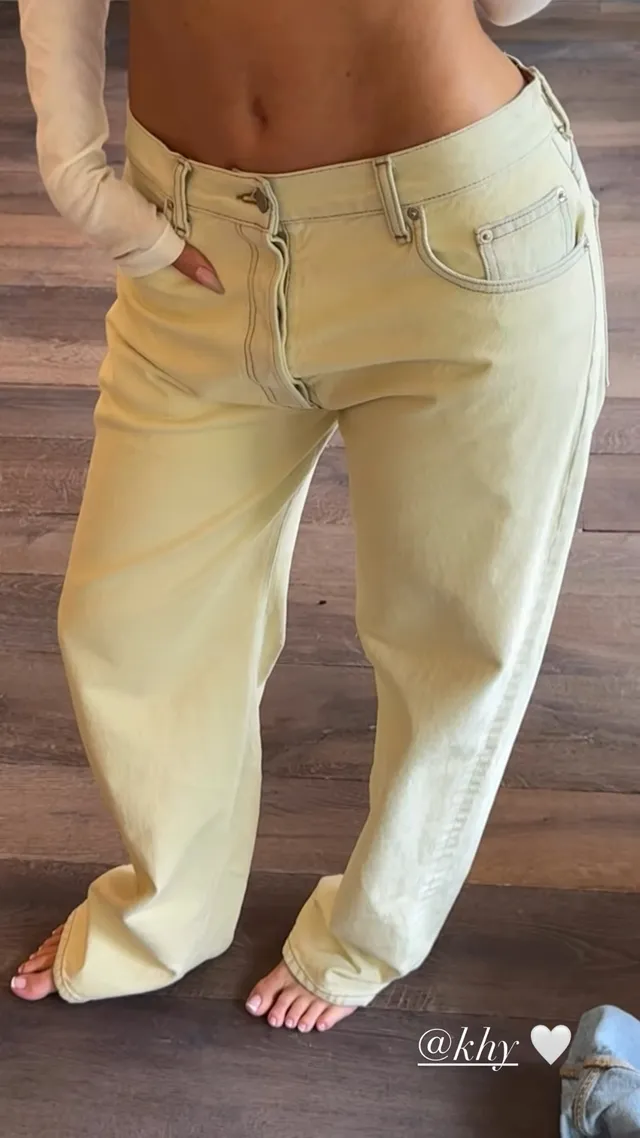 Kylie Jenner standing barefoot in pale yellow jeans.