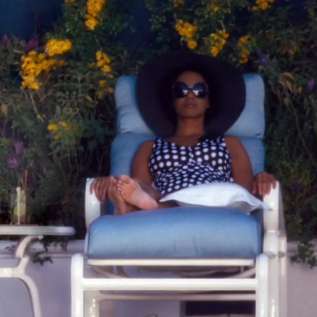 Zoe Saldaña relaxing on a garden lounger with a wide brimmed hat.