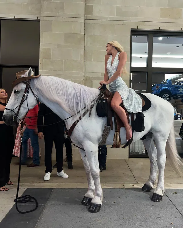 Olivia Dunne sitting on a white horse inside a stable.
