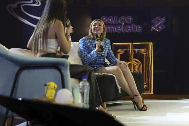 Peyton List sitting in a blue dress and black heels onstage.