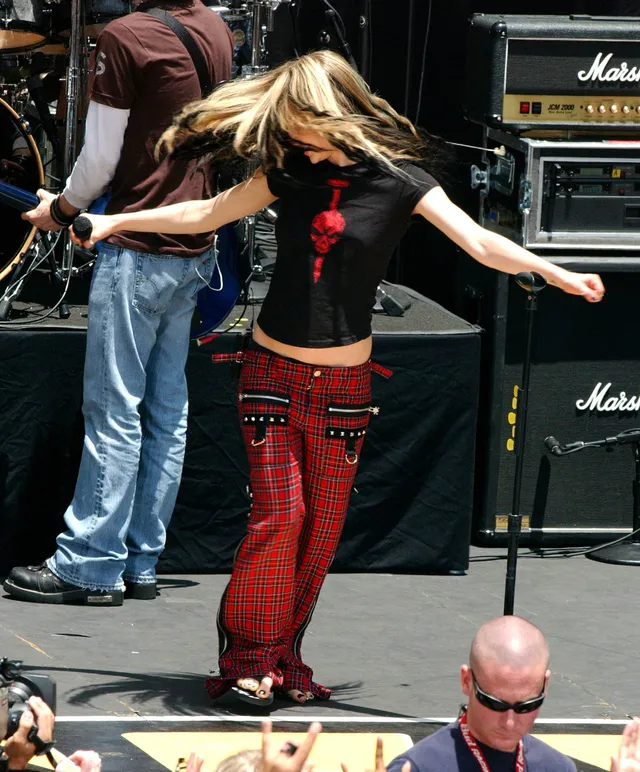 Avril Lavigne performing on stage in red trousers and flat sandals.