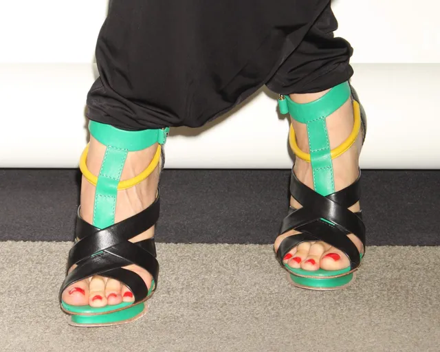 Gwen Stefani wearing colourful strappy heels beneath dark trousers.