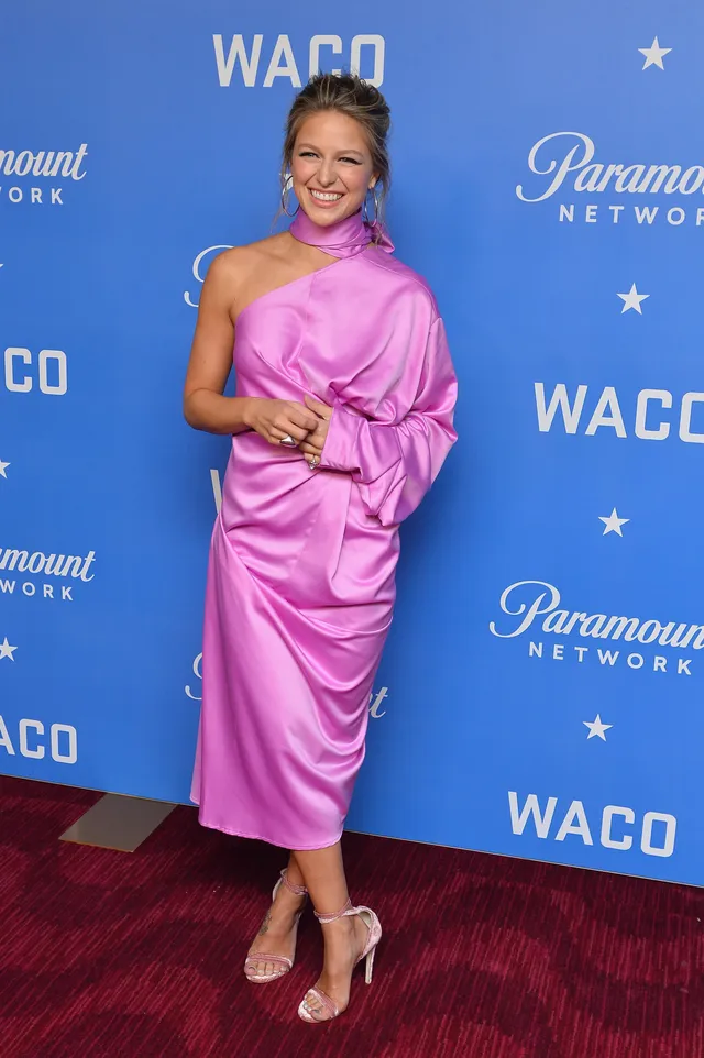 Melissa Benoist posing in a pink dress and pale heels at an event.