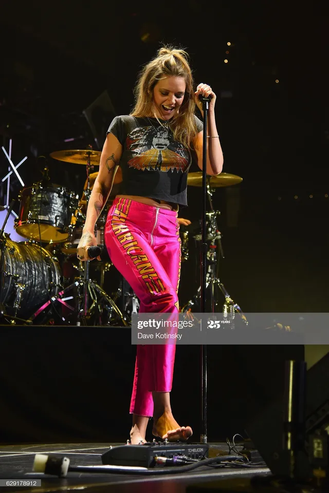 Tove Lo standing barefoot on stage in pink trousers.