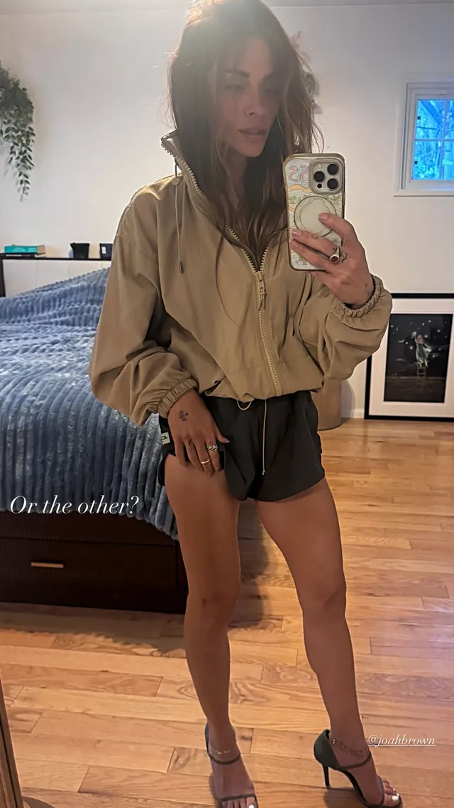 Sarah Shahi taking a mirror portrait in a shirt and dark shorts.