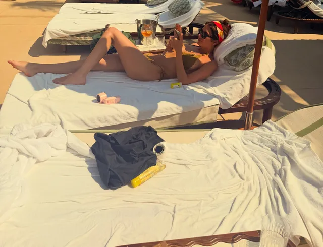 Ashley Benson reclining on a beach lounger in a hat.