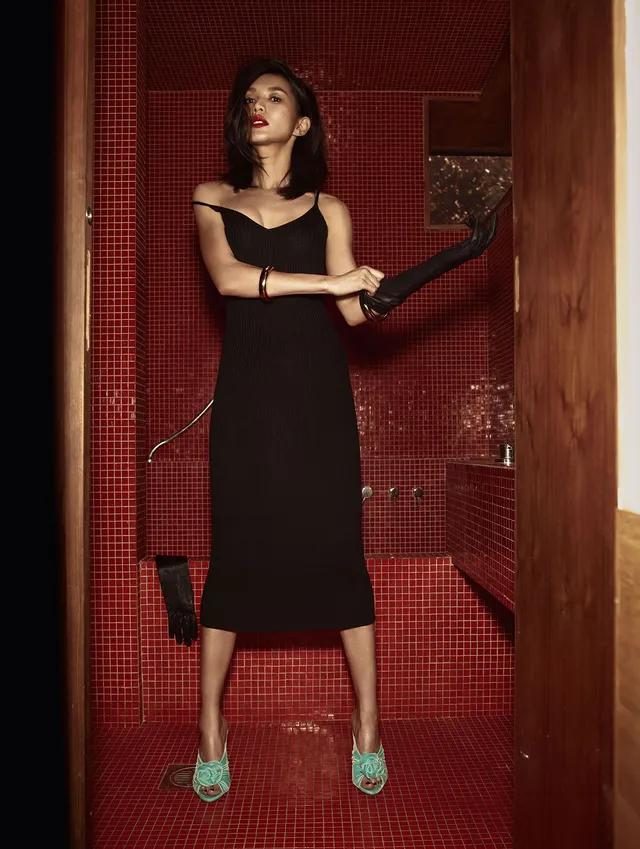 Gemma Chan posing in a tiled doorway in a black dress.