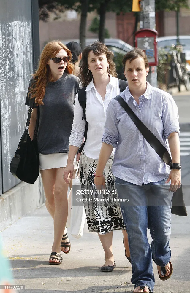 Kirsten Dunst walking outdoors in a dark top and pale shorts with companions.