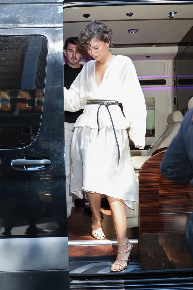 Zendaya stepping from a vehicle in a pale dress and gold heels.