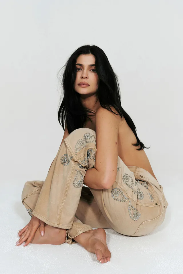 Kylie Jenner crouching barefoot in jeans for a studio portrait.