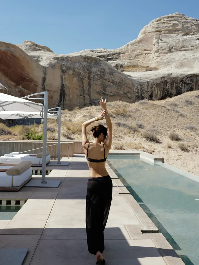 Lisa (Lalisa Manobal) standing barefoot beside a pool in black trousers and a dark top.