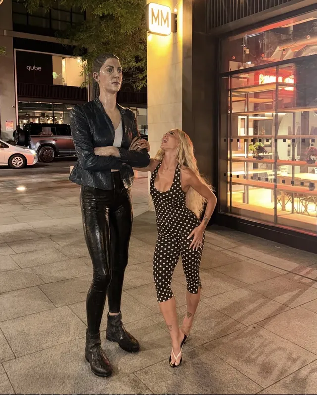 Alisha Lehmann wearing heeled sandals and a black patterned dress beside a companion.