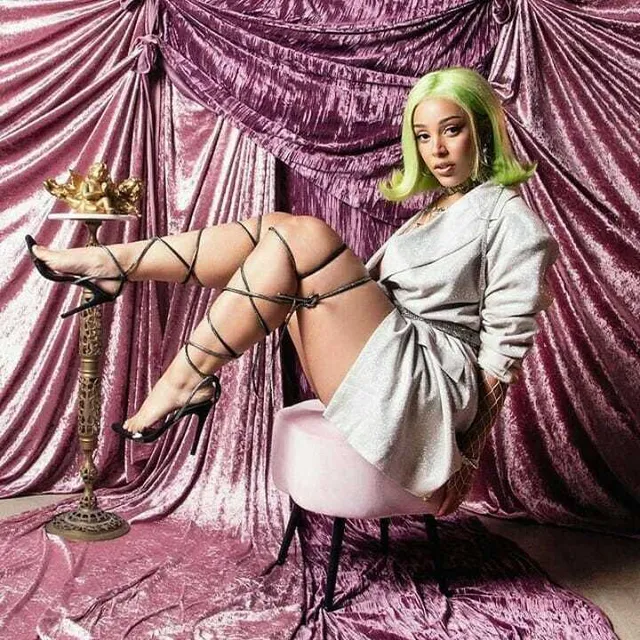 Doja Cat sitting in a grey outfit and black lace-up heels.