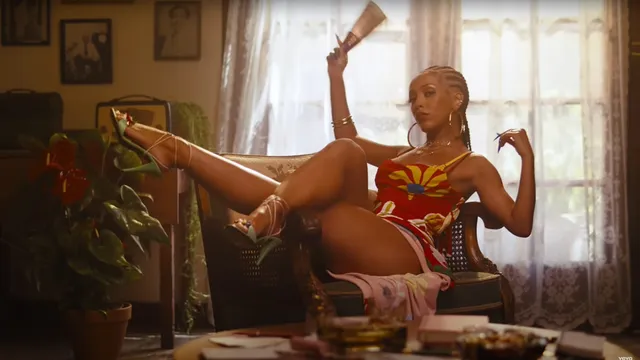 Doja Cat sitting indoors with a heeled shoe raised.