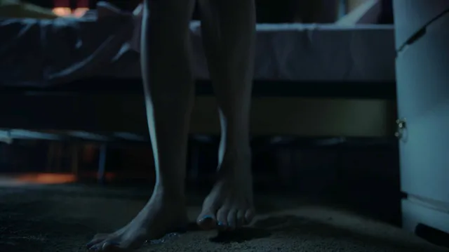 Peyton List standing barefoot beside a bed in a screen scene.