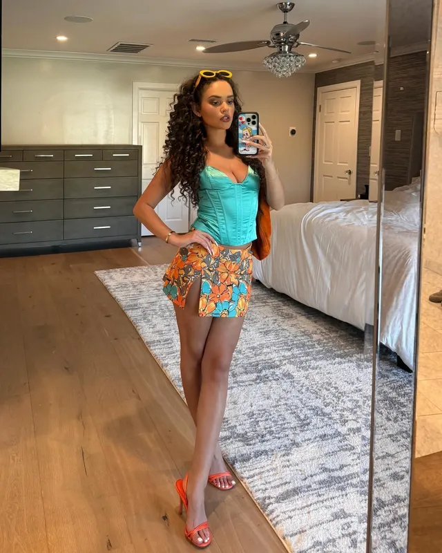 Madison Pettis taking a mirror selfie in a turquoise top, patterned skirt and orange heels.