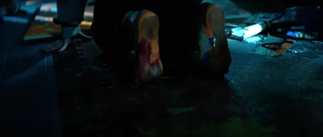 Sophie Thatcher raising bare soles from a blue-lit floor in a film scene.