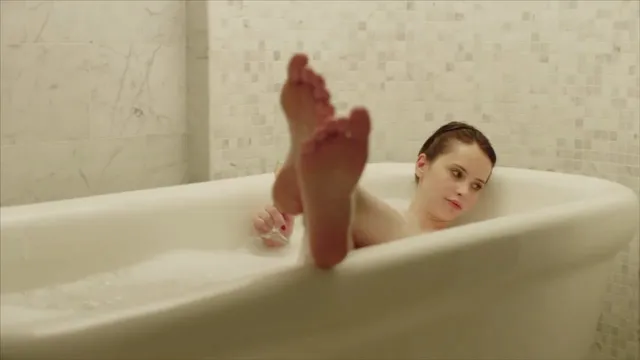 Felicity Jones raising her feet from a bathtub in a screen scene.