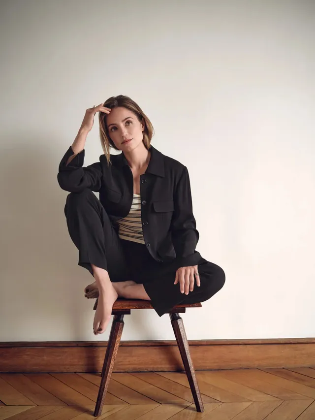 Dianna Agron sitting on a stool in a dark outfit for a portrait.