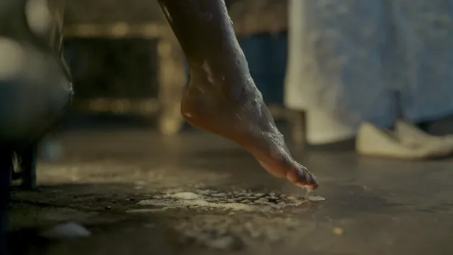 Freya Allan stepping barefoot on a wet indoor floor in a film scene.