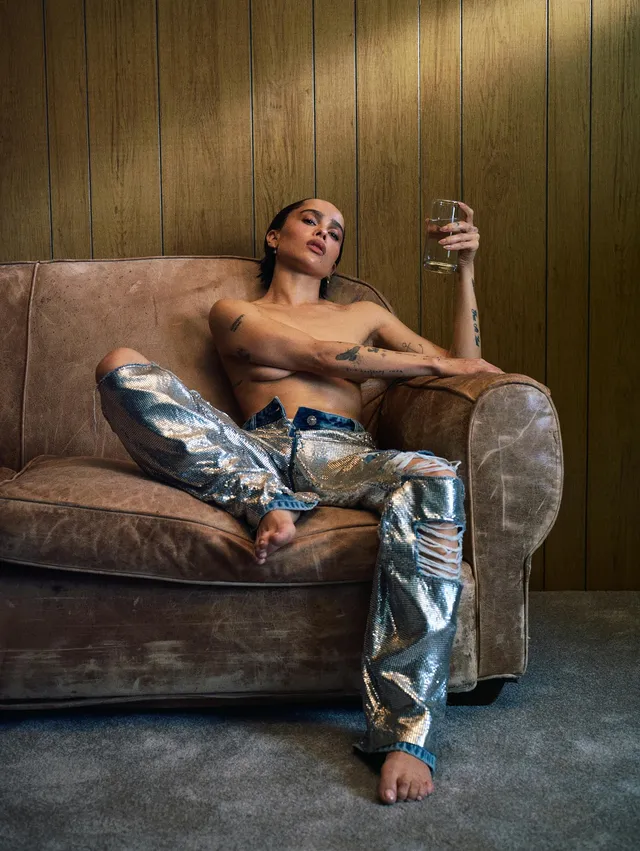 Zoë Kravitz sitting in an armchair in metallic trousers.