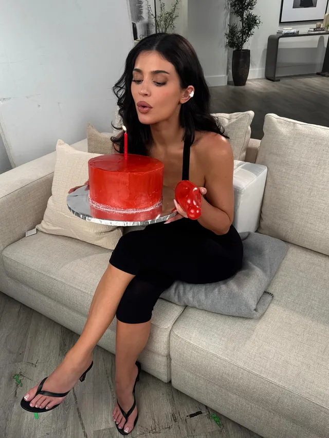 Kylie Jenner sitting on a sofa with a cake while wearing flip-flops.