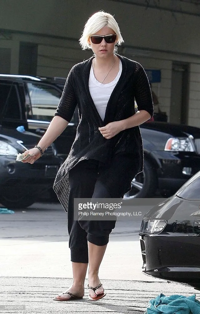 Elisha Cuthbert walking outdoors in cropped trousers and flip-flops.