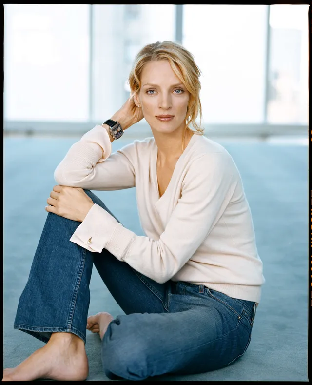 Uma Thurman sitting barefoot in a white top and jeans.