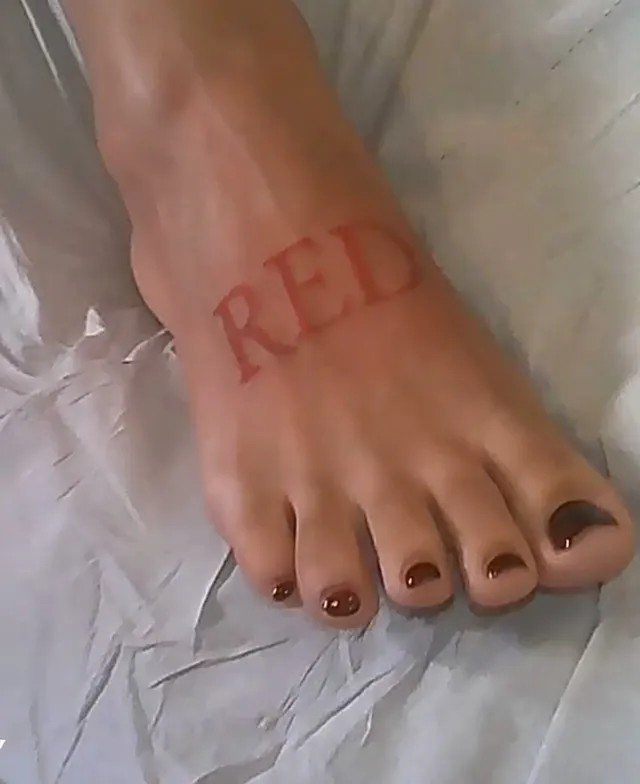 Doja Cat showing a bare foot with dark nail polish and red lettering.