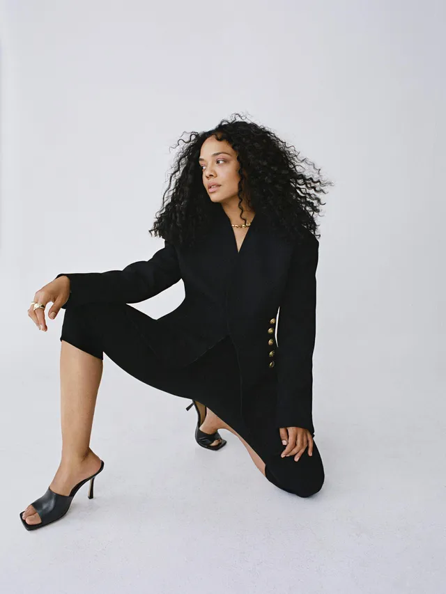 Tessa Thompson crouching in a black suit and heeled mules.