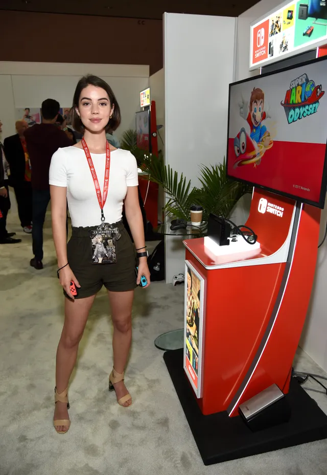 Adelaide Kane standing at a gaming event in shorts and heels.