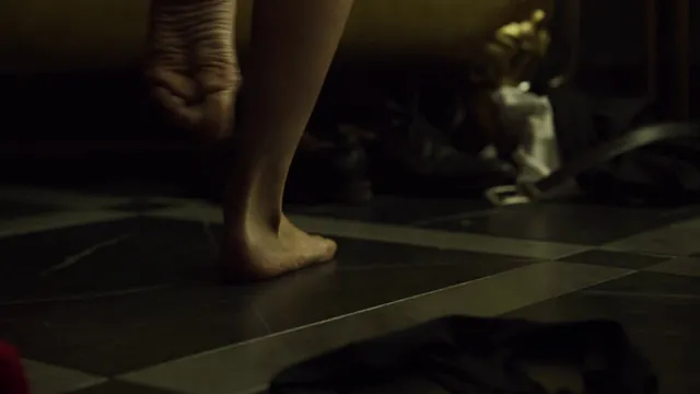 Úrsula Corberó shown standing barefoot in a dimly lit room in a scene.