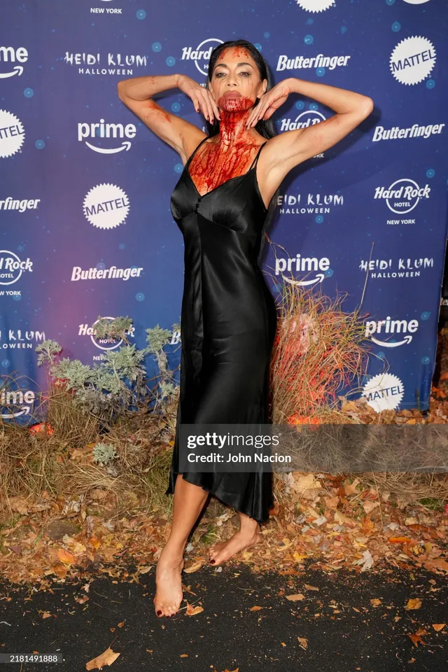 Nicole Scherzinger posing barefoot at an event in a black dress.