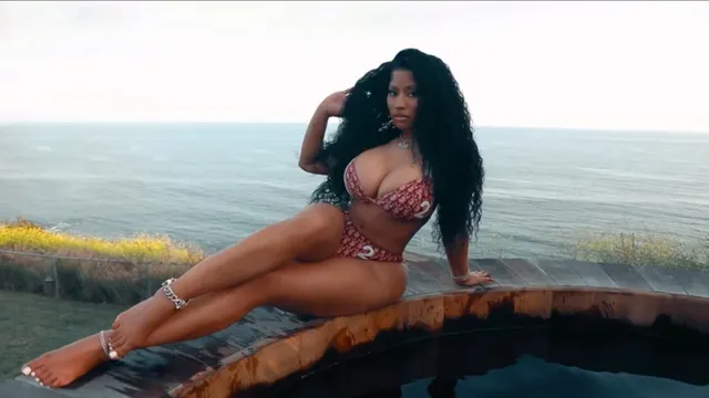 Nicki Minaj sitting barefoot beside a swimming pool.