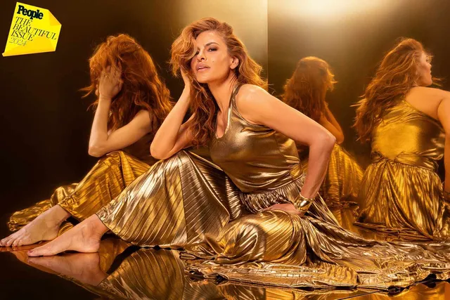 Eva Mendes sitting on a reflective floor in a gold dress.